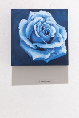 White and blue rose painting on a dark blue background on a square piece of wood with a black text caption printed on the wall below the painting