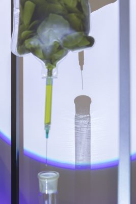 Close up An IV bag filled with green liquid and leaves connected to a syringe dripping