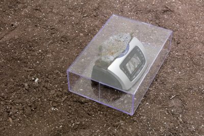 An electronic device in an acrylic box on top of a bed of dirt