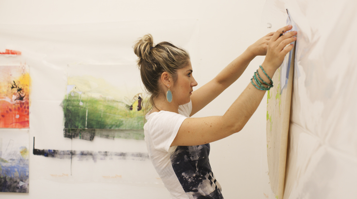 A student is installing a painting on a wall covered with white fabric