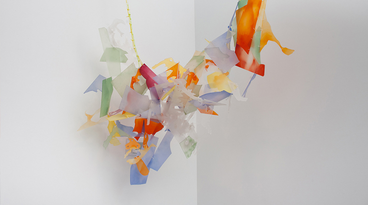 abstract sculpture made of scattered pieces of red, orange, blue, and green organic material suspended on the air with a thread