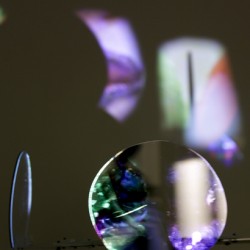 Organic rounded shape sculpture made of a translucent material and reflective surface with a projection of an image on it and the dark wall in the background