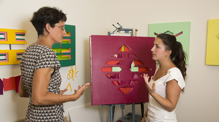 A teacher talking with a student in front of a maroon painting on the easel