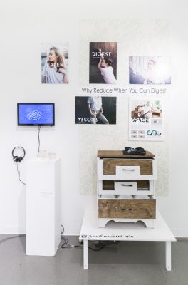 Gallery view with five photographs of various shots of people wearing a white shirt with white text over the images, a tv screen on the left with headphones and a small white pedestal in front of it with small sculptural pieces on top, to the left there is a small table displaying a small dresser that is white and raw wood
