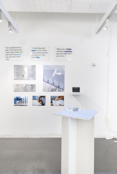 Installation shot of text on a wall and posters in the background, with a pedestal in the foreground.