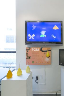 Installation shot of a pedestal with three pears in front of a TV screen displaying bugs on a blue background.