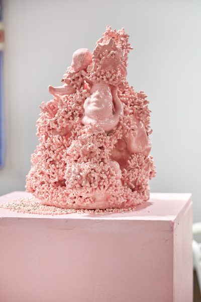Detail image of pink clay sculpture. Sculpture appears to be a combination of coral-like surface area and baby doll portions.