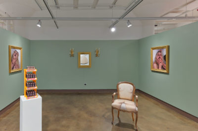 Installation view of photographic portraits hanging on a mint green wall with a chair in the center of the room that has been re-upholstered with photos of the body