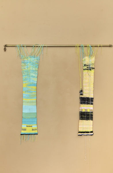 Two textile artworks hanging on a brass bar.