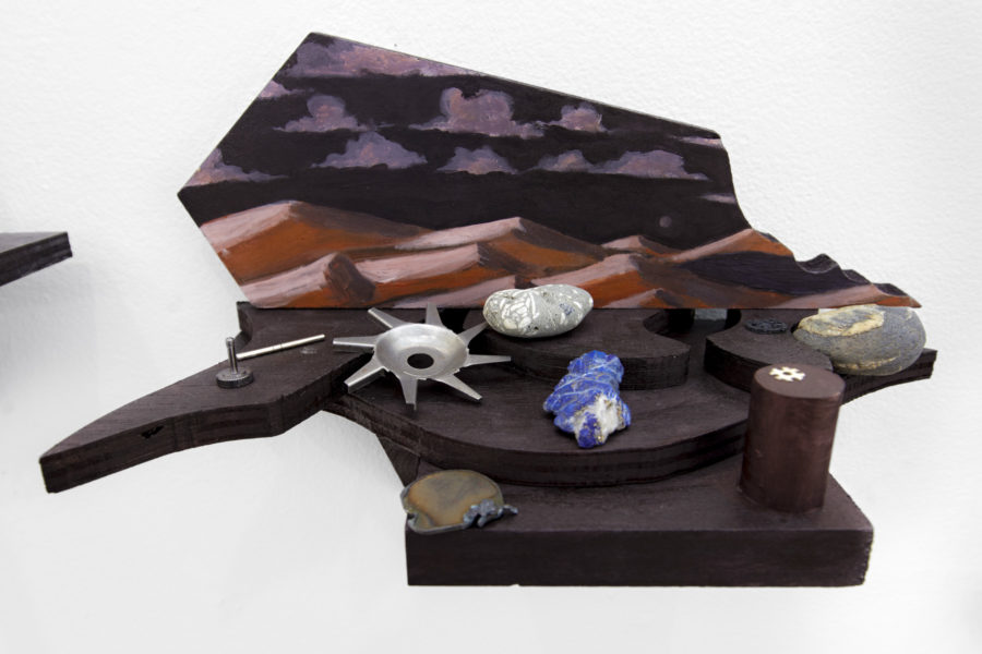 Sculpture made out of wood that is painted, landscape imagery, multiple objects placed on the sculpture.