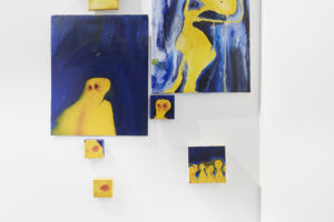 Artwork by Nancy Razk. BFA Fine Arts, 2019. Multiple paintings of a abstract yellow figure and a blue background.