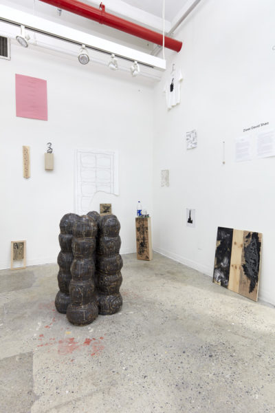 Artwork by Ziwei David Shao. BFA Fine Arts, 2019. Installation view. Large sculpture of multiple spheres carved out of wood. Multiple works on paper and canvas hanging on the wall. Wooden painted object laying against the walls.