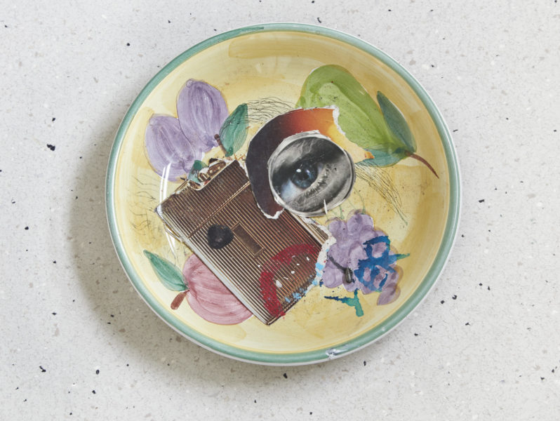 A collage using an image of an eye and another image of an object placed inside a ceramic plate that has flowers painted on it.