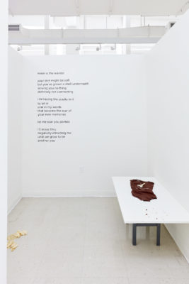 Large vinyl text is on the wall of white room with a shallow table in the corner