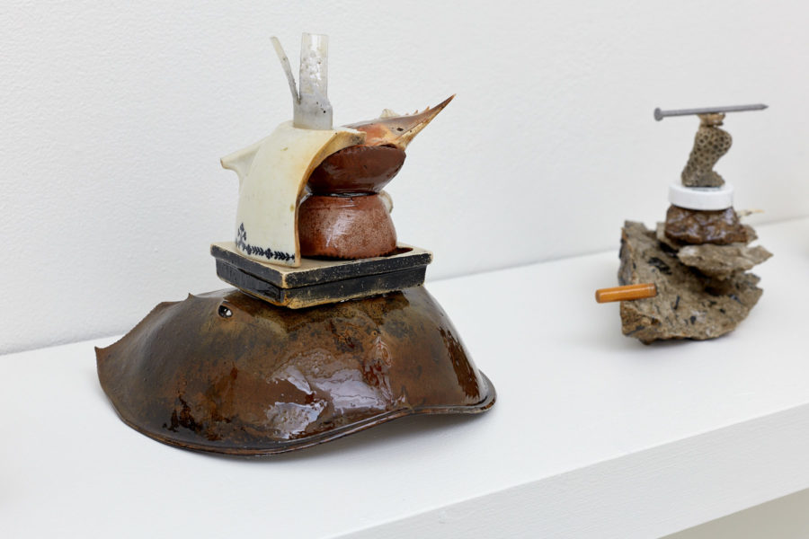 Two sculptures composed of neatly stacked found objects, such as crab shells, cigarette butts, nails and coral