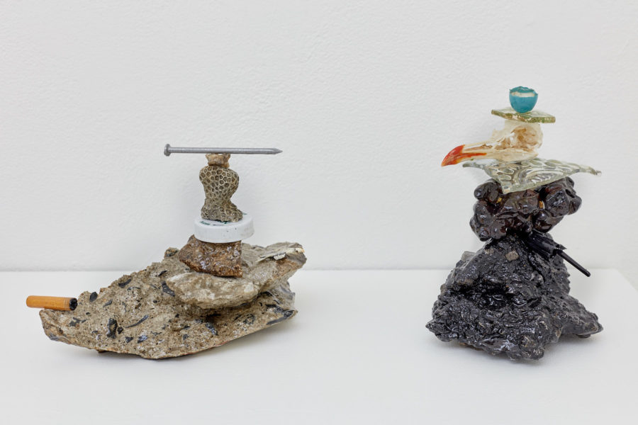 Two sculptures composed of neatly stacked found objects, such as cigarette butts, nails, coral, bottle caps and broken glassware