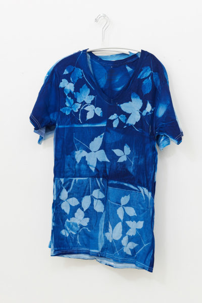 A dark blue t-shirt with a bleached leaf pattern hangs on a white wall