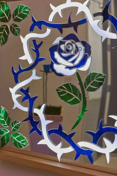 Close up of a laser cut mirrored lightbox that depicts a wreath of thorns with a rose in the center