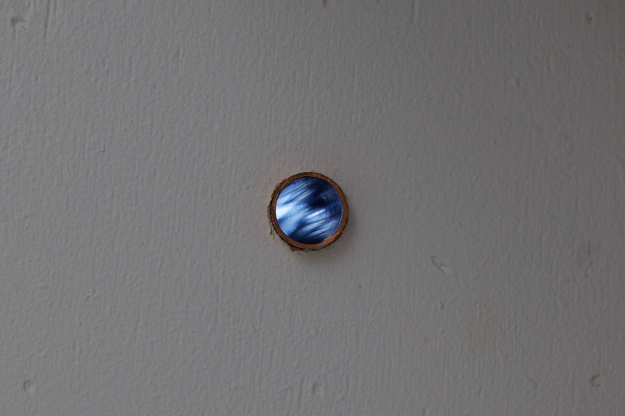 The rim of a copper pipe sticks out from a white painted wall, reveling a light inside