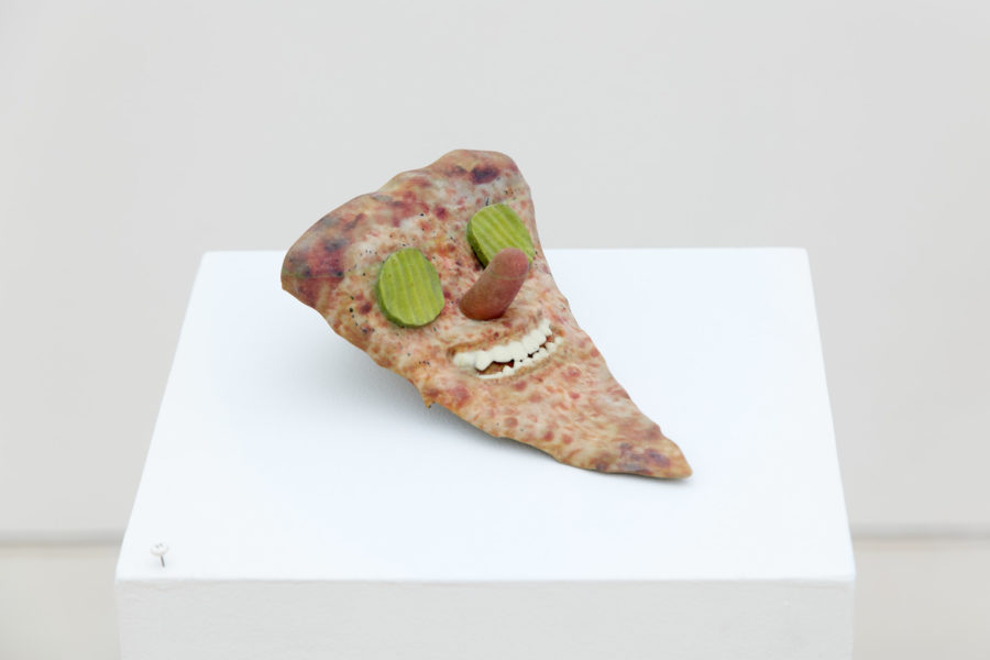 Exhibition "Tales and Whispers" 2019. SVA Flatiron Gallery, New York. Artwork by Titus McBeath. 3d printed pizza slice with pickles representing eyes, a hotdog nose and teeth.