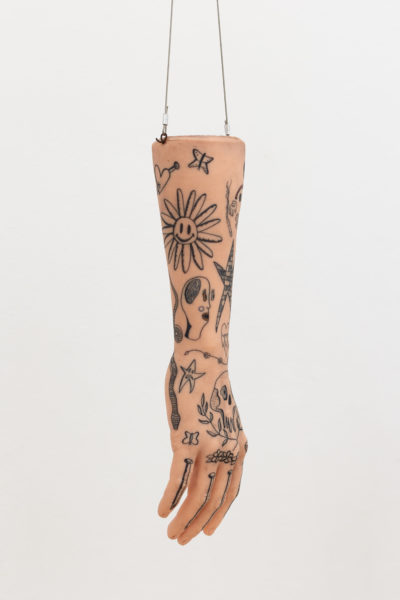 Exhibition Tales and Whispers 2019. SVA Flatiron Gallery, New York. Detail of artwork by Gregory Coscia.  A flesh colored arm with tattoos hanging from a wire..