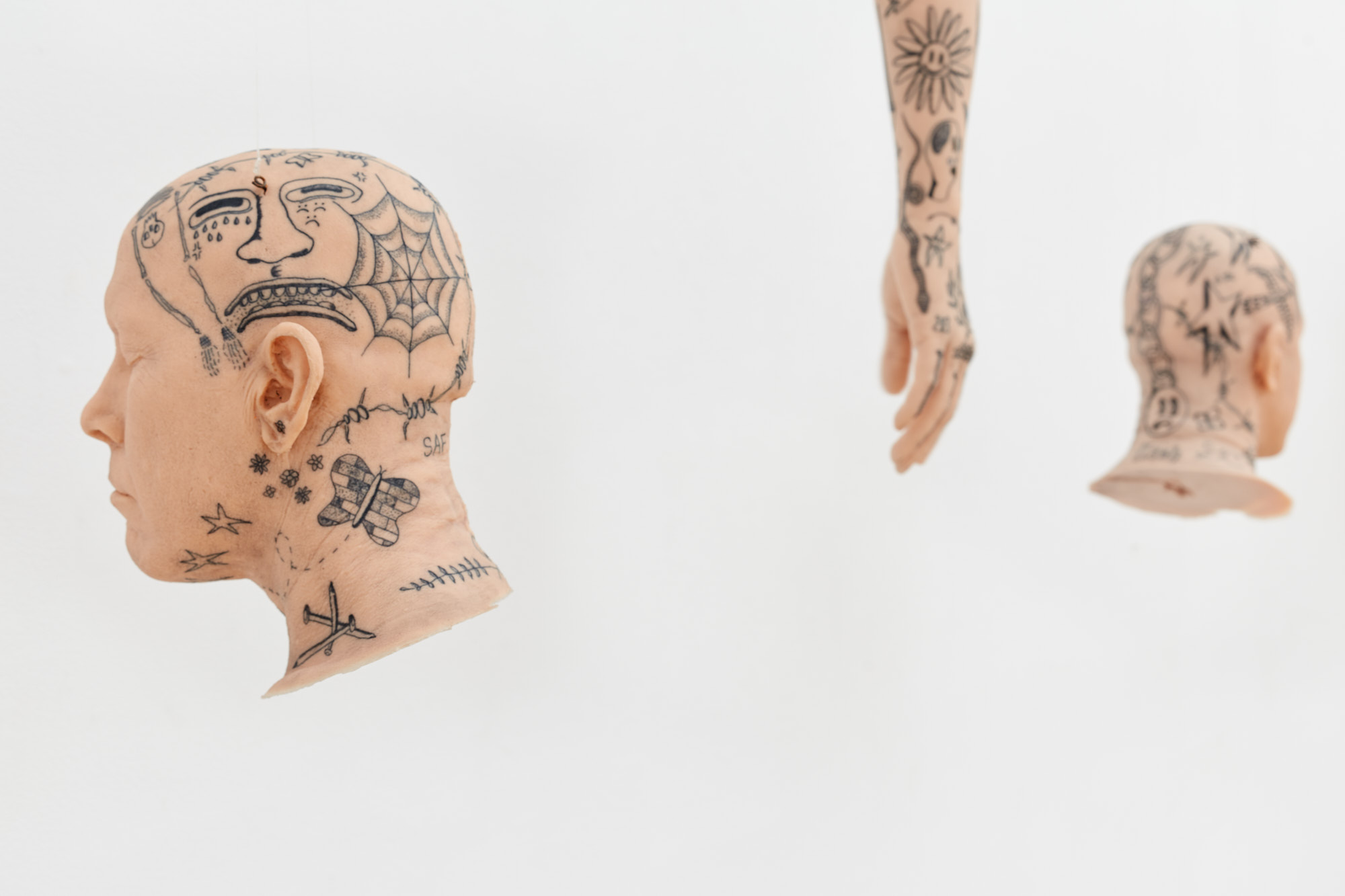 Exhibition Tales and Whispers 2019. SVA Flatiron Gallery, New York. Detail of artwork by Gregory Coscia. Two flesh colored sculptures of heads with tattoos and a flesh colored arm with tattoos.