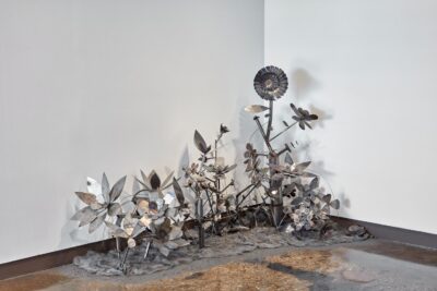 Metal sculpture of plants and flowers installed on the floor.