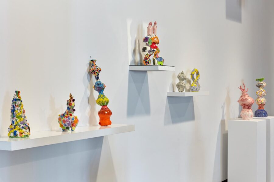 Installation view of 8 colorful ceramic sculptures on shelves and pedestals