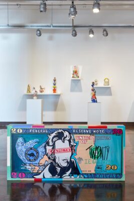 Installation view with a large bill note sculpture on the floor and ceramic organic pieces on the background. 
