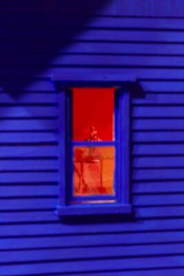 Detail of a window of a doll house with a ballerina in the interior. The facade is painted in deep ultramarine blue and the interior in saturated red.