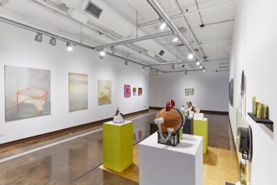 Installation view of a few pedestals with different sculptures and abstract paintings hung on the wall on the left side.