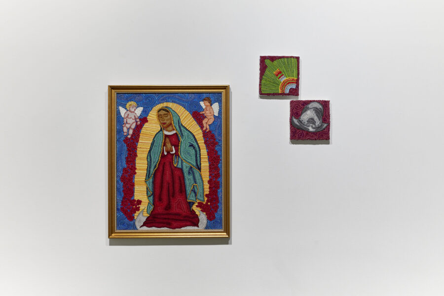 Installation view with three paintings depicting a virgin with two angels, a native american feathered headgear and a consquistador helmet