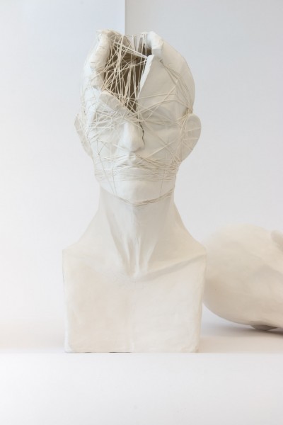 Facial expression sculpted in ceramic with an opening on the forehead while the head is tied-up with multiple layers of threads.