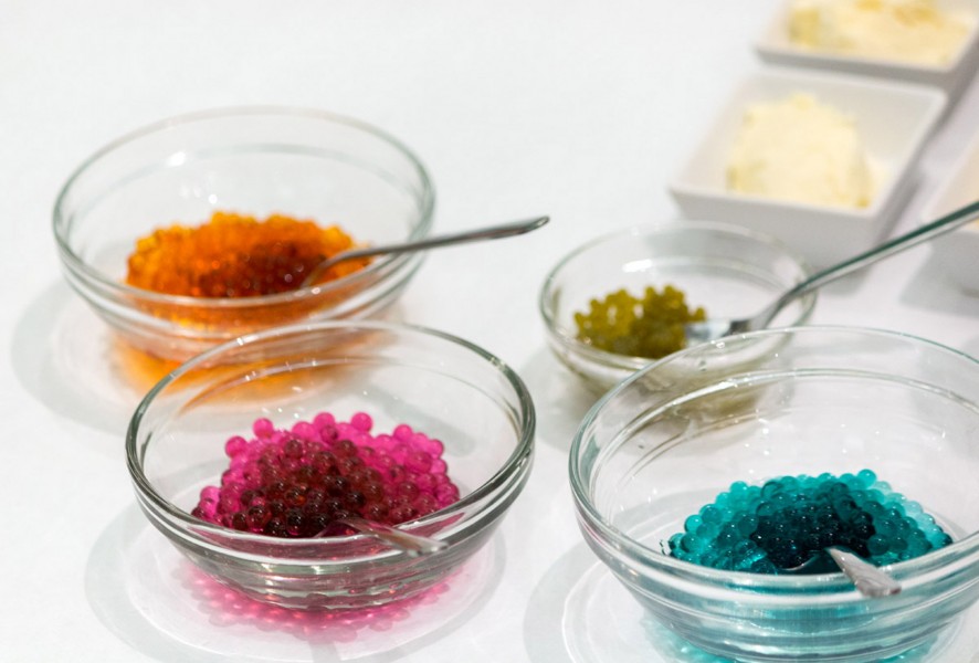 Four food bowls containing caviar roe in orange color, pink, olive, and blue.