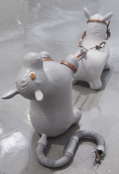 A sculpture cast in the shape of two Rodie bouncy rubber horse toys, in gray material. The front horse has a leather bridle, the straps of which are held by the back horse.