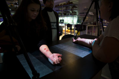 Audience engaging in interactive projection of two arms undergoing medical procedure onto the surface of a black table