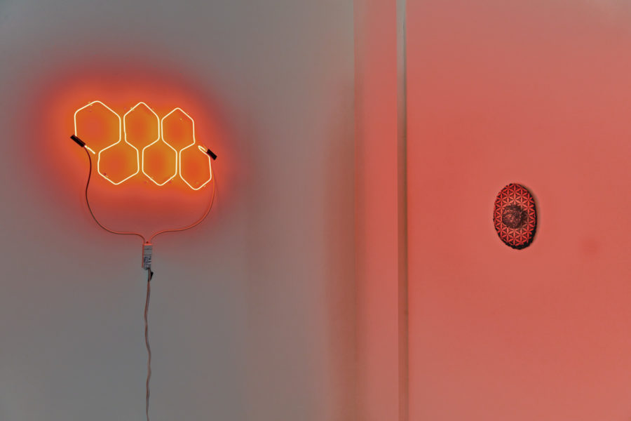 Artwork by Melissa Rose Pressler. BFA Fine Arts, 2019. Installation view. Circular mixed media artworks hanging on the wall. Neon sign with six orange hexagons.