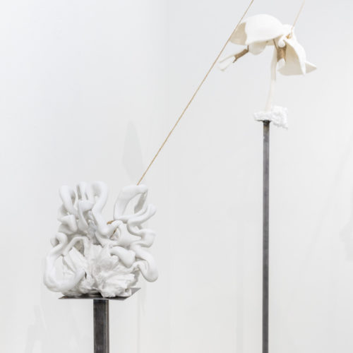 Multiple ceramic sculptures balancing on thin metal pedestals held in place by thick thread.