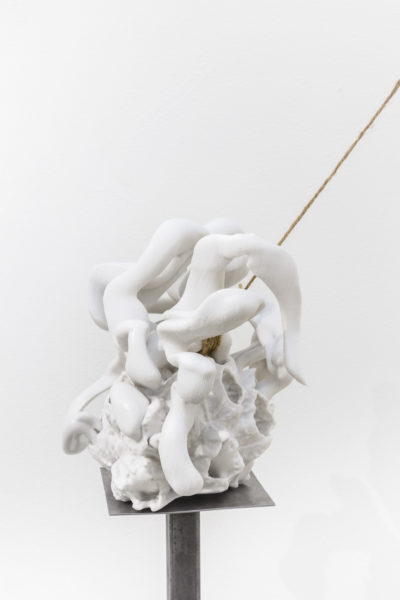 Ceramic sculptures balancing on thin metal pedestals held in place by thick thread.