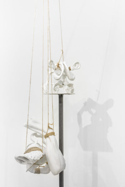 Multiple ceramic sculptures balancing on thin metal pedestals held in place by thick thread.