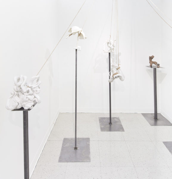 Multiple ceramic sculptures balancing on thin metal pedestals held in place by thick thread.  