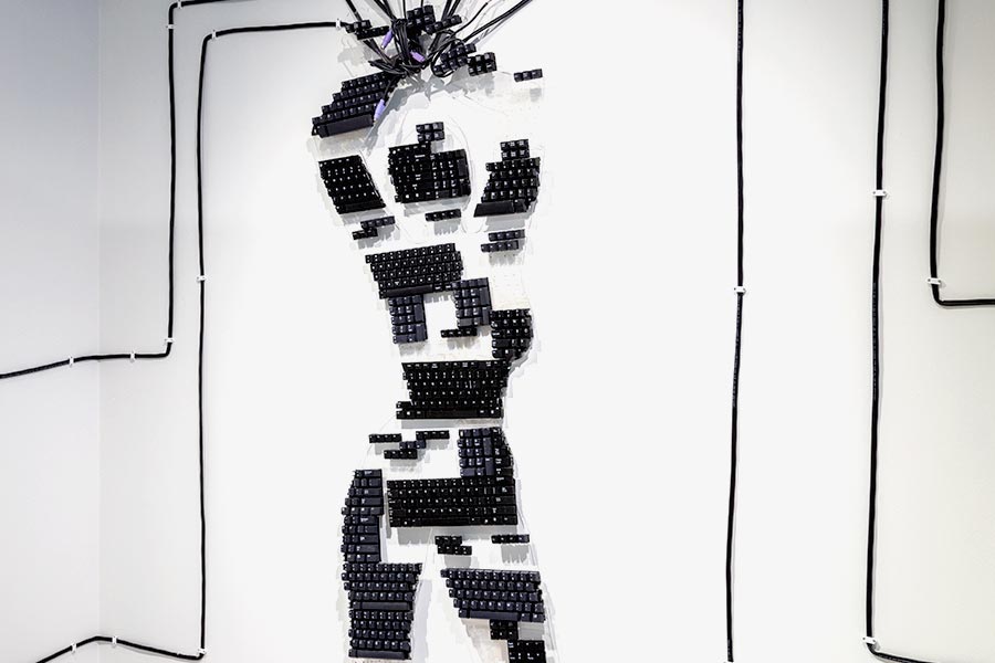 A wall installation of fragmented keyboards that depicts the female form with their arms suspended above their head
