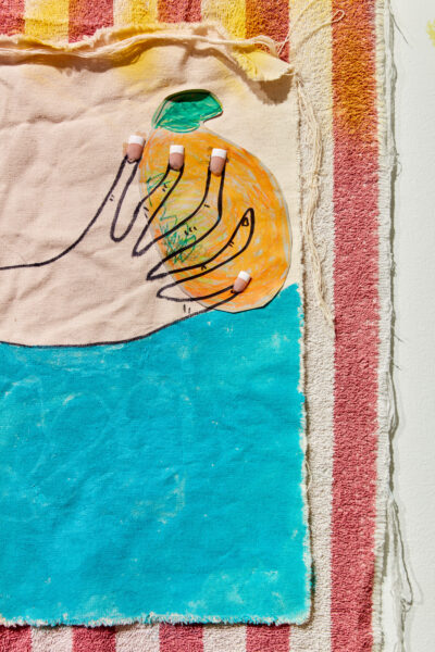 Detail shot of a multimedia work that shows a striped towel and canvas with a hand painted on it.