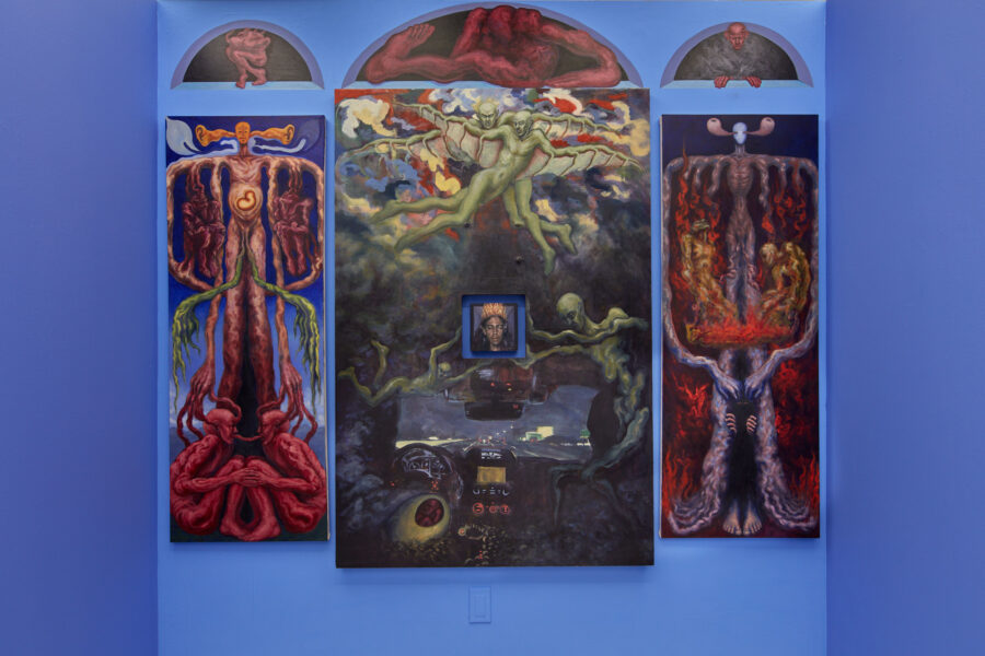 Four paintings hang on a blue wall. There is a large central painting with green figures floating around in abstract space. There is a square hole in the center of this painting that houses a smaller portrait. To the left and right of the central painting are two paintings with the same composition and identical figures but in different moments of time. Above the paintings there are three arched openings that have been painted onto the wall. Inside the openings are three separate figures.