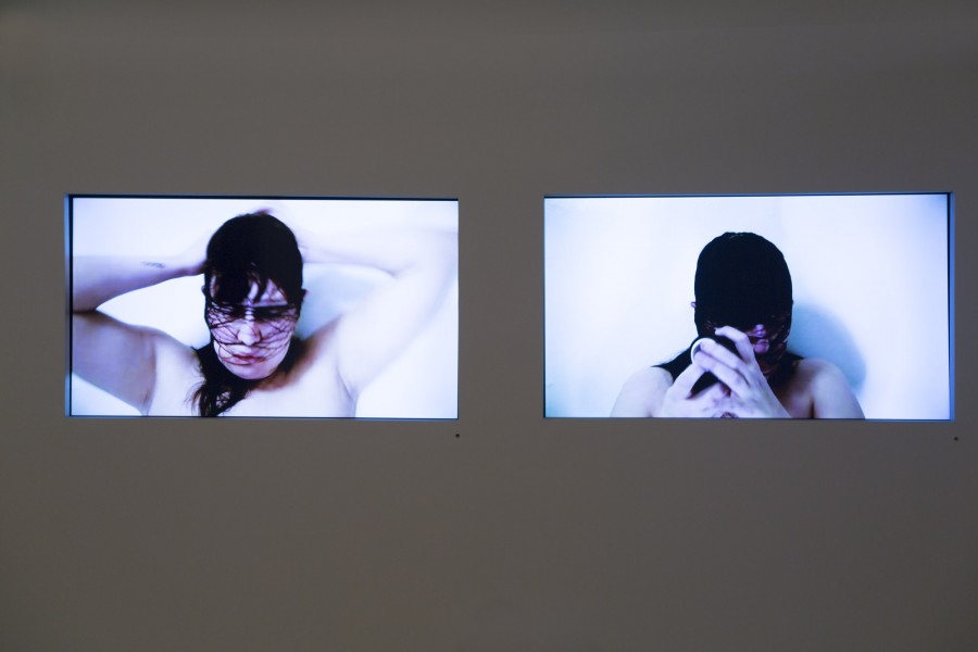 Two monitors showing a person wrapping her face with black thread.