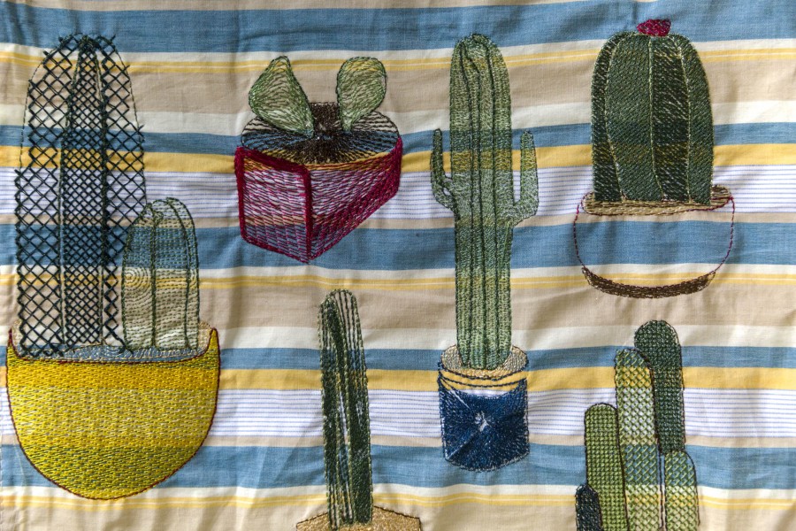 A close view of different cactuses sewed on a piece of cloth with horizontal colored cloth.