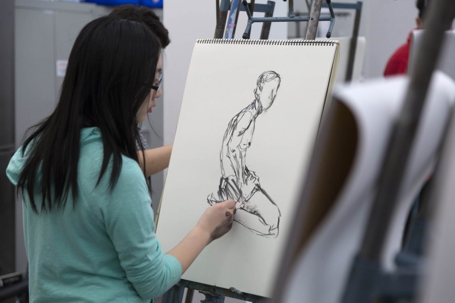 The student is drawing a sitting model with graphite at her easel.