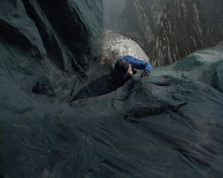 down looking view of a person with a blue suit, brown hat and gloves is climbing a rock wall