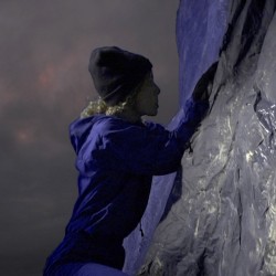 Profile view of a person with a blue suit, hat and gloves is climbing on a rock wall