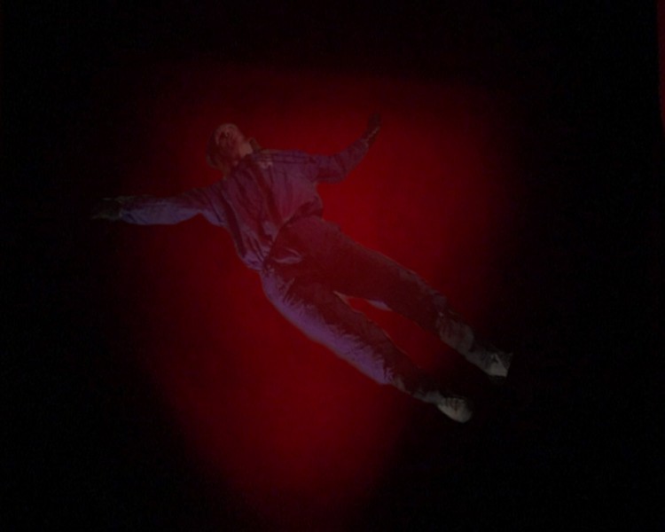 A person with a blue suit floating with a red light in the middle of the frame and black background.